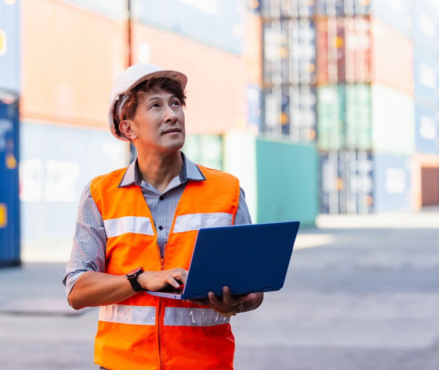A foreman in a hard hat checking a laptop in a container yard